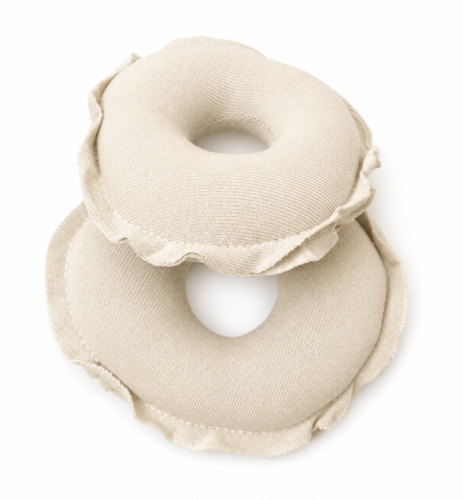 Um par de rosquinhas de amamentação protetoras de seios feitas de tecido de algodão texturizado na cor bege claro e off-white, com acabamento em babados nas bordas, sobre um fundo branco limpo